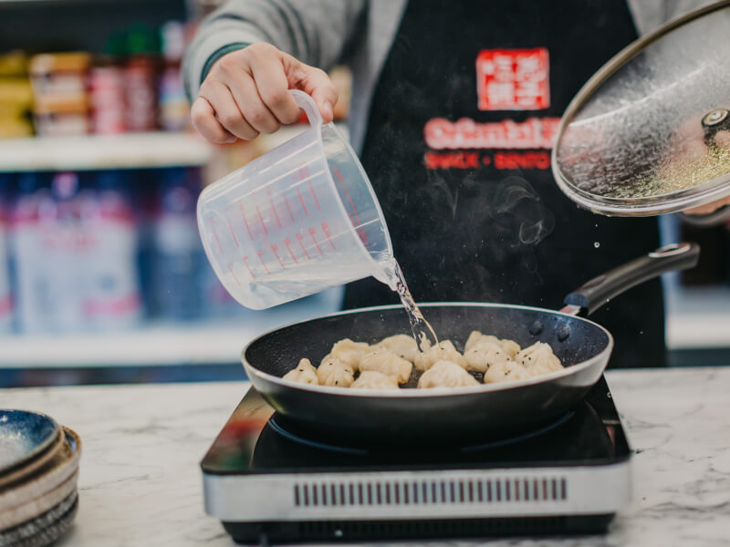 A man pouring water into a pan with dumplings